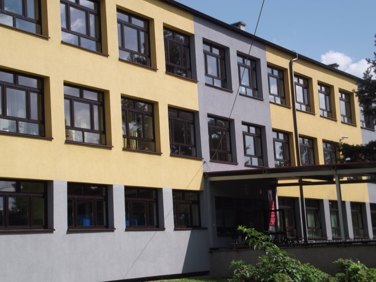 Trzykondygnacyjny budynek z elewacją w kolorach żółtym i szarym. Liczne prostokątne okna w ciemnych ramach. Wejście główne z zadaszeniem wspartym na metalowych słupach. Przed budynkiem roślinność.